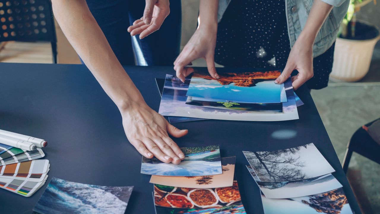 Two people collaborating over photo prints on a table indoors.